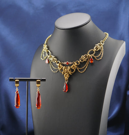 A gold-toned chain necklace and matching drop earrings displayed on a black mannequin bust, set against a draped blue satin fabric background.