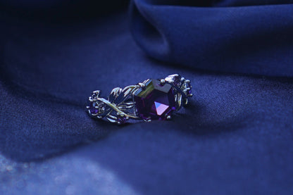  a small silver ring featuring a purple crystal resting on top of blue satin.