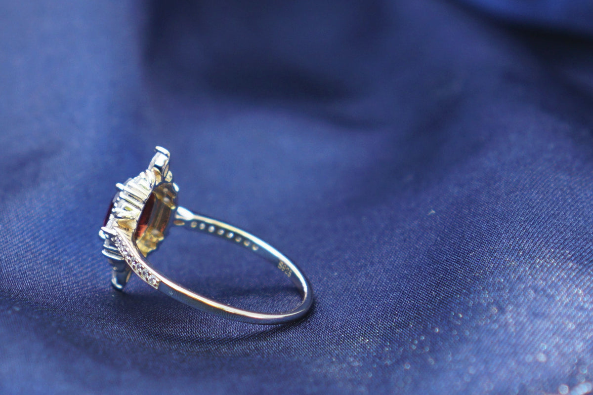 A gold ring with a clear gemstone resting on draped dark blue fabric.