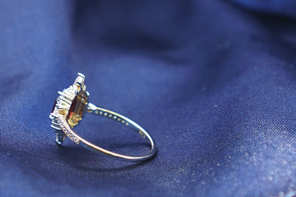 A gold ring with a clear gemstone resting on draped dark blue fabric.